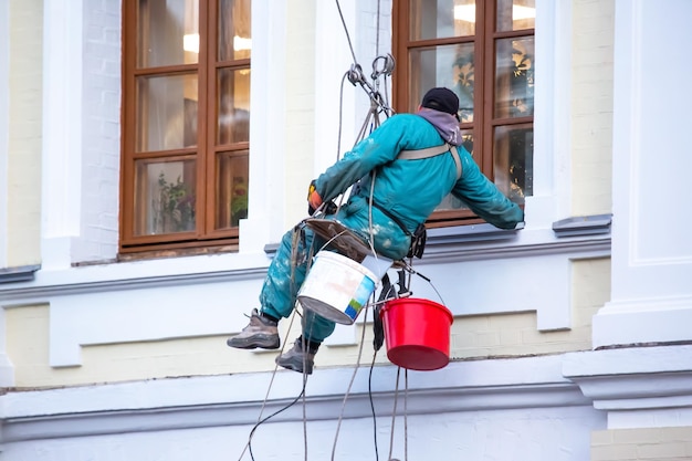 Climber worker is engaged in the repair and cleaning of windows and the facade of a renovated residential building construction business industry