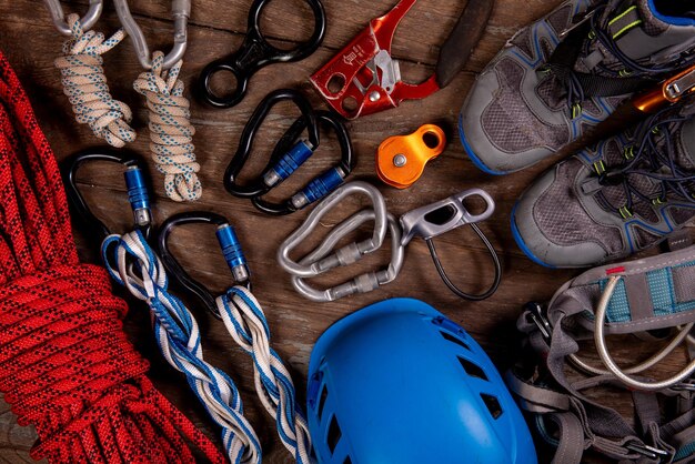 Climbing equipment for mountaineering and hiking helmet hammer carabiner trekking shoes and other on wooden background top view