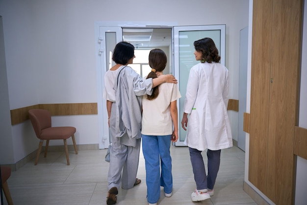 clinic employee accompanies young patient with her mother to procedure
