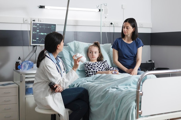 Clinic pediatric specialist recommending ill patient girl right\
medicine for illness remission. hospital pediatrist specialist\
talking with attentive mother about illness treatment.