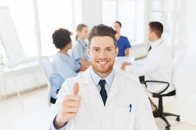 Photo clinic, profession, people, gesture and medicine concept - happy male doctor over group of medics meeting at hospital showing thumbs up gesture