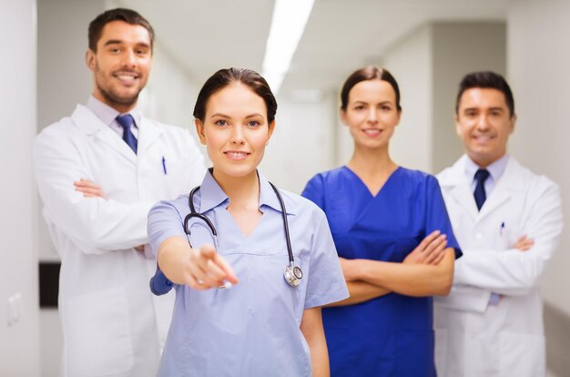 clinic, profession, people, health care and medicine concept - group of happy medics or doctors pointing finger on you at hospital corridor