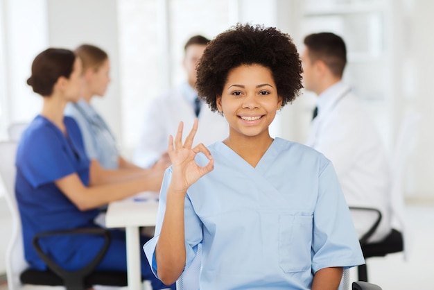 診療所、職業、人、医学のコンセプト – 病院で会った医療関係者のグループの上に幸せな女性医師が、OKの手話を示している