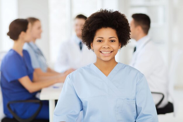 Clinic, profession, people and medicine concept - happy female\
doctor or nurse over group of medics meeting at hospital