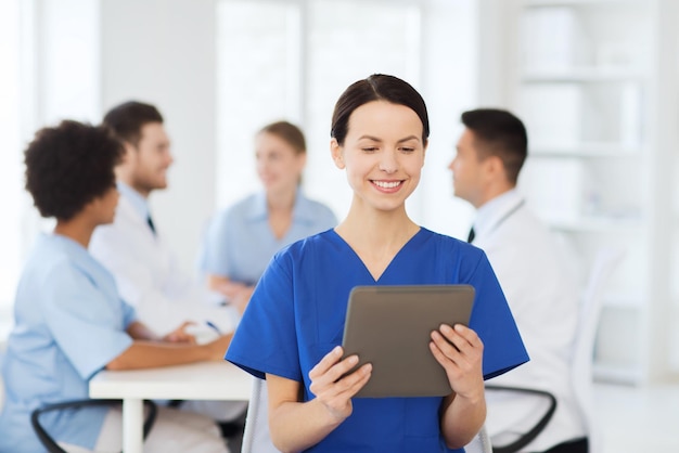 Clinic, profession, people and medicine concept - happy female\
doctor with tablet pc computer over group of medics meeting at\
hospital