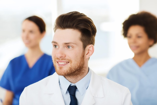 Clinic, profession, people and medicine concept - happy male\
doctor over group of medics meeting at hospital