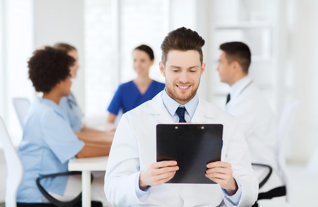 Clinic, profession, people and medicine concept - happy male\
doctor with tablet pc computer over group of medics meeting at\
hospital