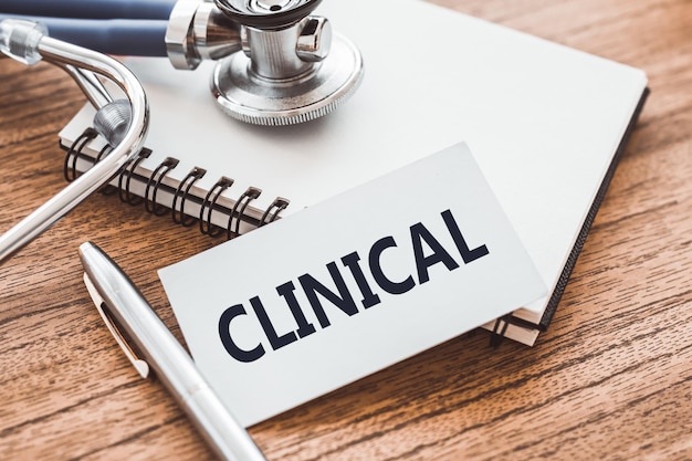 CLINICAL text on card on wooden table with stethoscope and notepad for medical records