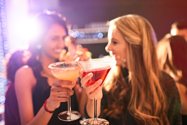 飲む前にチャリンという音を立てるパーティーでカクテルを飲む2人の若い女性のショット