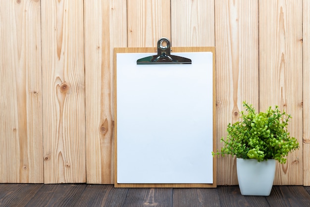 Clipboard blank white paper sheet with little decoration tree in white vase on wooden background