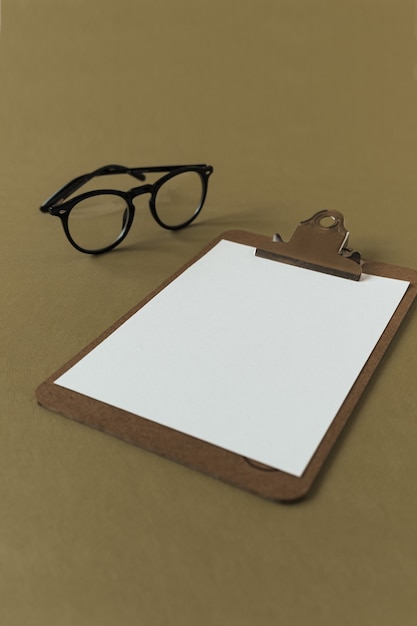 Clipboard pad with blank paper sheet and glasses on olive surface