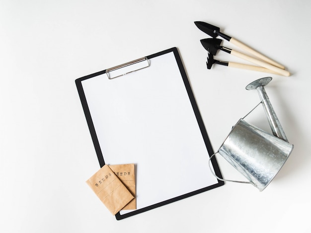 Clipboard and paper for text, garden tools and seeds in paper bags on white