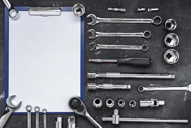 Clipboard surrounded by wrenches and other car repair tool on a dark background