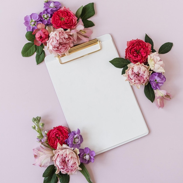 Blocco per appunti per tablet con foglio di carta bianco su tavolo rosa neutro area di lavoro della scrivania dell'ufficio di casa dell'artista estetico con boccioli di fiori di rosa mockup di vista dall'alto piatto con spazio vuoto per la copia