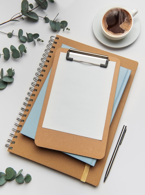 Clipboard with blank paper notebooks and coffee cup on white table