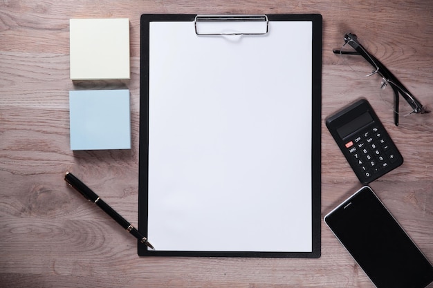 Clipboard with blank sheet and business items on wooden background