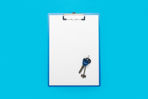 Photo clipboard with a blank sheet and keys to the house or apartment on a blue