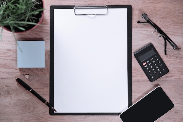 Clipboard with blank sheet smartphone and calculator on wooden b