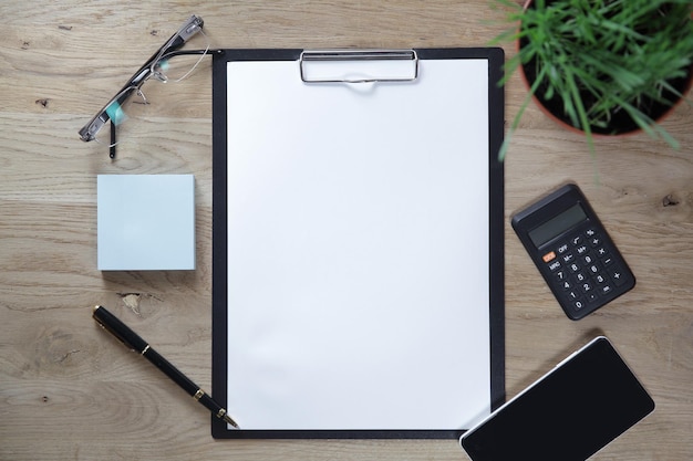 Clipboard with blank sheet smartphone and calculator on wooden b