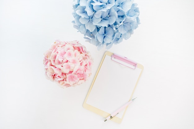 Clipboard with copy space and pale pastel hydrangea flowers bouquets on white surface