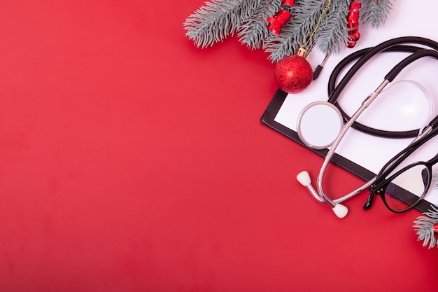 Clipboard with medical stethoscope, glasses, christmas tree on red background with copy space. Medical christmas concept