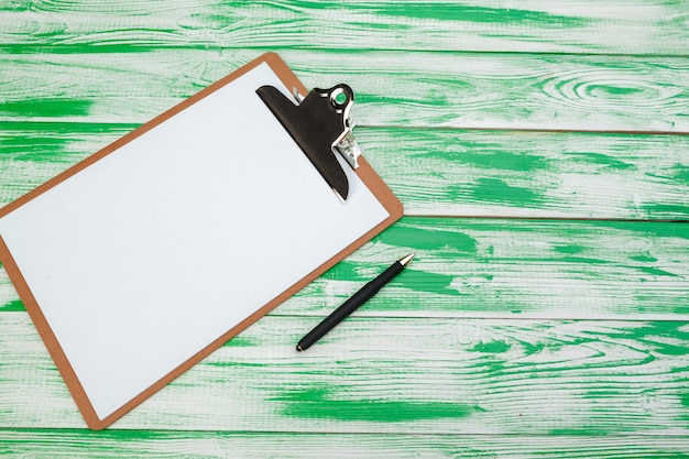 Clipboard with office supplies on green wooden table