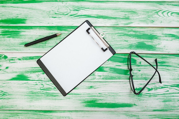 Clipboard with office supplies on green wooden table