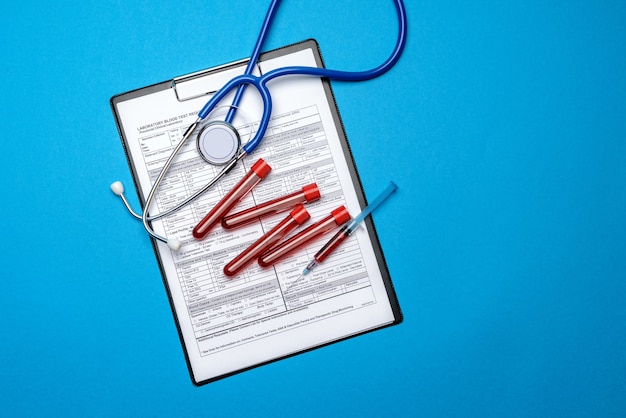 Clipboard with paper blank form with medical tools on blue background with cope space.