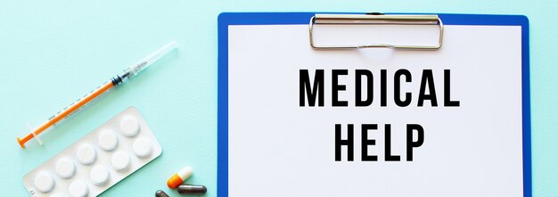 A clipboard with paper lies on a table near drugs and a syringe. Inscription MEDICAL HELP.