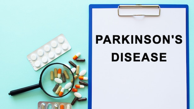 A clipboard with paper lies on a table near drugs and a syringe with PARKINSONS DISEASE inscription