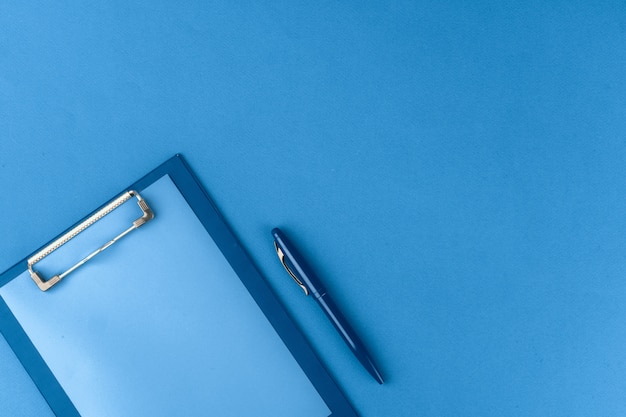Буфер обмена с ручкой на синем фоне, вид сверху
