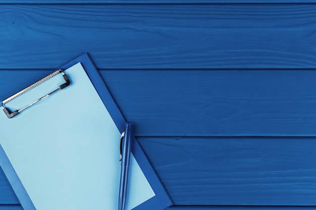 Clipboard with pen on blue table, top view