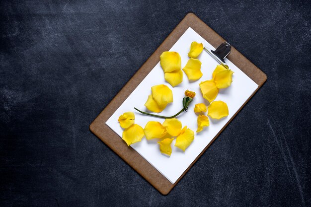 Clipboard with and a Petal of yellow rose on black background. Valentine's Day