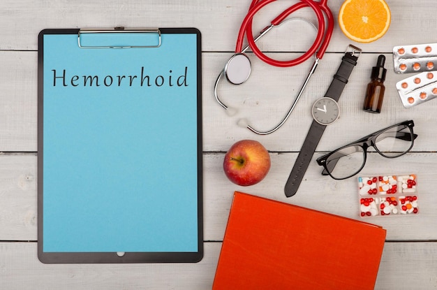 Clipboard with text Hemorrhoid pills stethoscope book fruits eyeglasses and watch