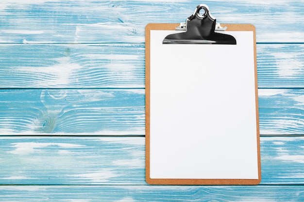 Photo clipboard with white blank paper on blue wooden table