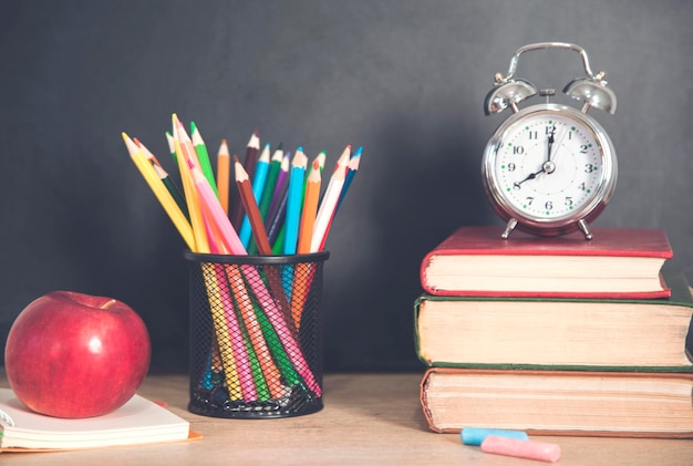 Clock on books with pencils and apple