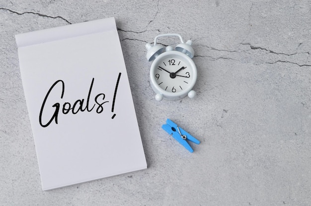 時計の洗濯ばさみとテキスト「GOALS」が書かれたノート