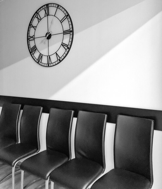 Clock over empty chairs arranged against wall