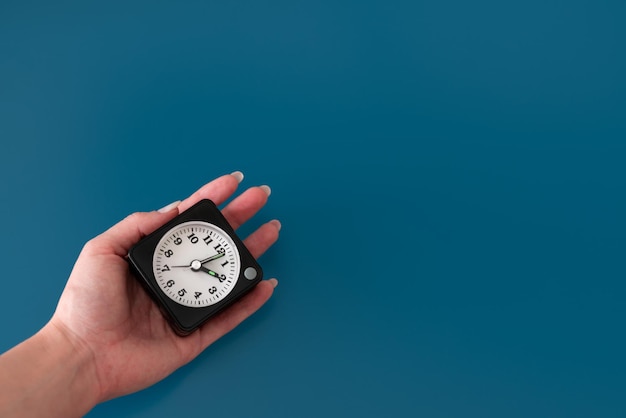 Clock in a female hand on blue isolated background. Hand holding watch