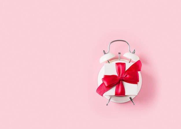 Clock gift on pink background, top view, copy space