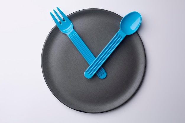 Clock grey plate with plastic spoon and fork eating time meal concept