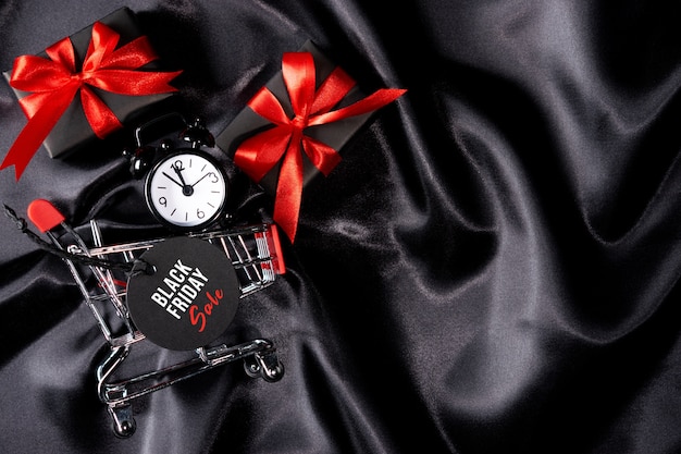 Clock in shopping cart with black tag and gifts on black fabric.