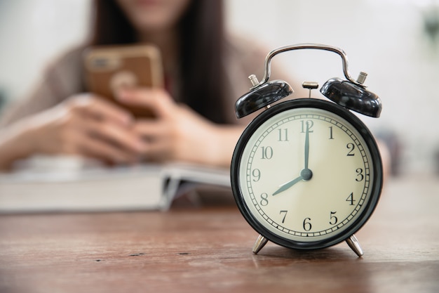 Photo clock with blur girl teen playing smartphone while reading book for waste time