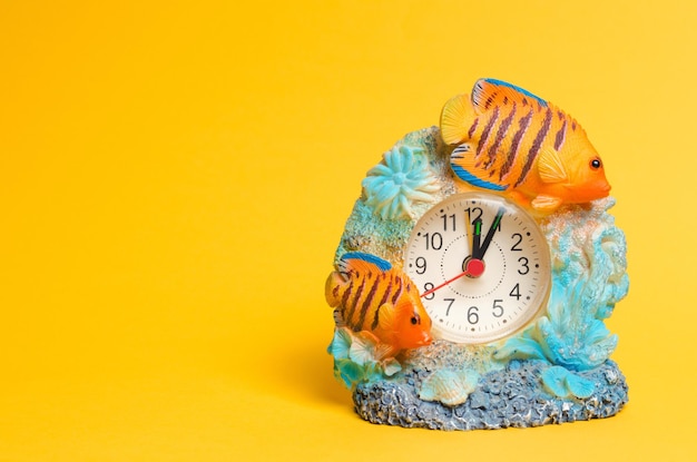 A clock with fish on a yellow background a place for text summer time arrow points to the beginning of the first alarm clock