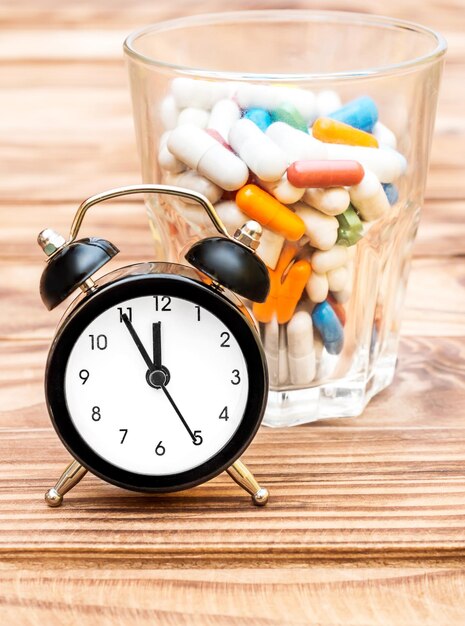 Photo clock with full glass of pills on the table medical concept