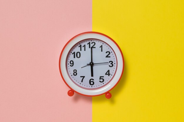 Clock with hands on a yellow and pink background.. Classic analog clock.