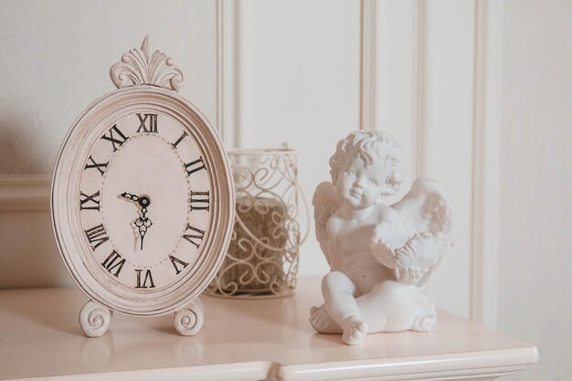 A clock with roman numerals on it next to a vase and a statue of a cherub.