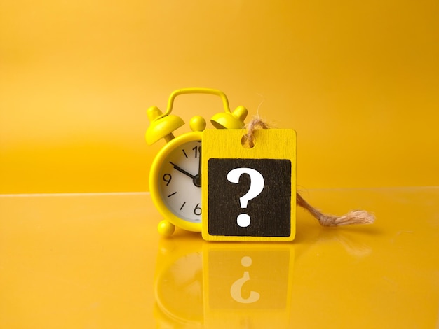 Clock and wooden board with question mark symbol on a yellow background