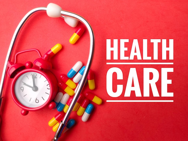 Clockstethoscope and pill with text health care on red background