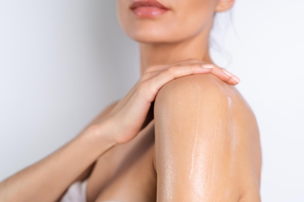 Close beauty portrait of topless woman with perfect skin holding bottle of shampoo lotion apply on shoulders and body on white background